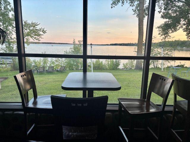 Empty table and chairs by a window overlooking a lake and trees at sunset.